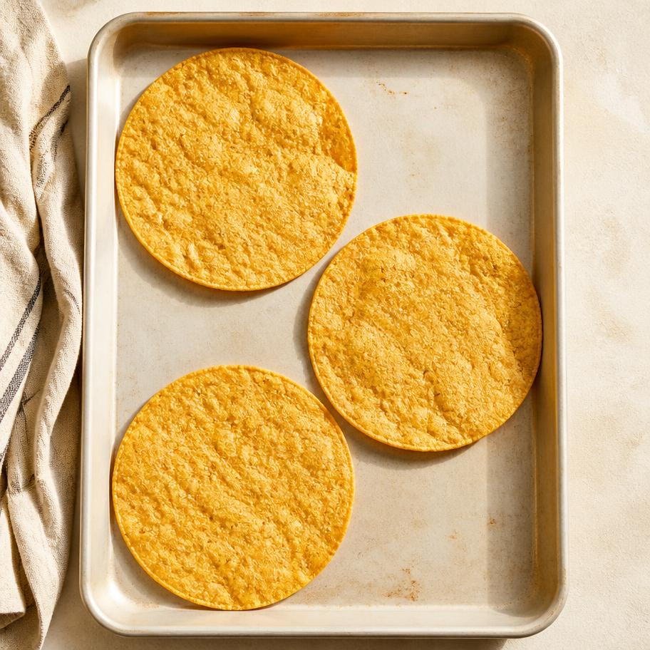 Three plain flat golden corn taco shells warming on a baking sheet